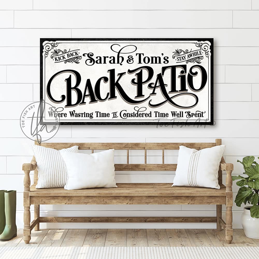 Welcome to the Back Patio personalized wall sign by Toe Fish Art in vintage black and white scroll style, available in framed canvas or waterproof outdoor metal, with custom family name and fun sayings like Kick Back, Stay Awhile, and Where Wasting Time is Considered Time Well Spent—charming backyard or patio decor handmade in the USA. Perfect for enhancing your outdoor summer decor. Built to last with genuine craftsmanship, this authentic sign adds rustic cottage charm and heritage quality to any home.