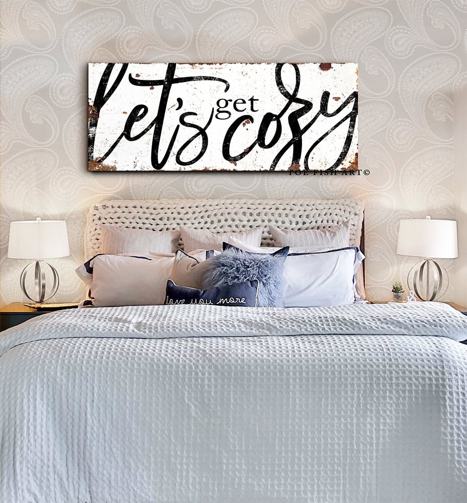 Toe Fish Art “Let’s Get Cozy” farmhouse wall decor sign in rustic white and black, available as a framed canvas or durable metal sign. Warm and inviting master or guest bedroom, living room, lounge, cottage style artwork adds rustic charm and modern country elegance to any space designed for snuggling. Handmade, authentic, heritage quality American-made wall art, perfect for farmhouse, cottage, or rustic industrial style home decorating.
