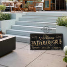 Welcome to the Patio Bar & Grill custom wall sign by Toe Fish Art, handmade in the USA in waterproof outdoor metal or framed canvas, vintage black with rustic gold, personalized family name text, and fun sayings like Kick Back-Stay Awhile, Sipping-Grilling-Chilling. Charming outdoor kitchen, bar, lounge, patio, lanai, deck, porch, or pool decor. Ideal for upgrading your outdoor summer vibe. Built to last with genuine craftsmanship, this authentic sign adds classic charm and heritage quality to any space.
