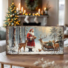 Toe Fish Art Santa Claus feeding reindeer in a snowy forest with sleigh and woodland animals, rustic Christmas wall art scene.