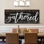 Toe Fish Art's rustic industrial sign "The Best Memories are Made Gathered Around the Table" in framed canvas or outdoor waterproof metal. This unique sign is hand-lettered by the artist, and features a rustic dark charcoal and rusty brown metal finish with striking white lettering, embodying a classic and timeless modern farmhouse cottage aesthetic. Available in a large selection of sizes, this handmade decor piece is proudly crafted in the USA, and ships free within the "lower 48" states. Blending rustic primitive country charm with modern cottage farmhouse style, this unique handcrafted artwork is made of durable high-quality framed canvas or outdoor weatherproof solid aluminum metal, making it perfect for incorporating in any remodeling, renovation or decor update project, indoors or outdoors. Proudly made in the USA, each piece is designed to last a lifetime by the artisans at Toe Fish Art. This beautiful sign enhances any decor, adding eye-catching appeal to your space. It’s perfect for your patio, lanai, bar & grill, deck, veranda, dining room, kitchen, or breakfast nook. A splendid reminder of time well spent with family and friends gathered 'round, this artwork fits various styles, including rustic modern farmhouse, cottagecore, vintage, retro, industrial, Americana, primitive, country, coastal, and minimalist. Toe Fish Art is a small family, woman-owned business, creating beautiful decor for almost three decades, since 1997!