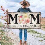 Toe Fish Art's unique, artisan-made Vintage Flower Bouquet "MOM" sign personalized with hand-lettered cursive family names to fit your style. This custom wall art is available as a wood-framed canvas with choice of framing colors, or outdoor waterproof metal, showcasing a worn rustic white background with bold black lettering and a beautiful painting of red, pink, and yellow roses. An ideal Mother's Day gift or any special occasion to celebrate Mom! Expertly made with American-sourced materials. This premium, handcrafted piece features a timeless aesthetic. Built to last with genuine craftsmanship, it adds rustic charm and heritage quality to any space. Made in the USA with durable, authentic materials for a beautiful and meaningful display. Rustic Cottagecore Country and Modern Farmhouse wall decor handcrafted in durable high-quality framed canvas or outdoor weatherproof solid aluminum metal, handmade in the USA from start to finish! Beautiful, stylish and timeless floral wall decor painting. Handcrafted in the USA by ToeFishArt, and built to last a lifetime by the Toe Fish Art family artisans. This beautiful original artwork adds unique eye-catching decor indoors or outdoors. Add instant outdoor curb appeal to your home! Perfect for your porch, entryway, patio, lanai, deck, garden, courtyard, gazebo, pergola, living room, fireplace hearth or mantel, wall hanging or shelf sitter, dining room or bedroom. This painting is a beautiful reminder of the gift of Mom's love to celebrate her for Mother's Day and all-year long. Original, custom, personalized wall decor signs. Canvas, Wood or Metal. Rustic modern farmhouse, cottagecore, vintage, retro, industrial, Americana, primitive, country, coastal, minimalist. Toe Fish Art is a USA small family woman owned business making beautiful decor since 1997.