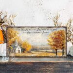 Toe Fish Art's Faith-inspired wall art featuring Psalm 107:1 ‘Give thanks to the Lord for He is good, His love endures forever’ hand-lettered on a rustic country church scene surrounded by golden autumn trees landscape painting. Handmade in the USA and constructed in framed canvas or waterproof outdoor metal. Vintage fall colors, perfect for Christian home décor, Thanksgiving, or seasonal autumn cottagecore decor.